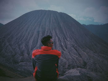 Rear view of man standing on mountain against sky