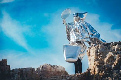 Low angle view of woman wearing costume standing on rock against sky