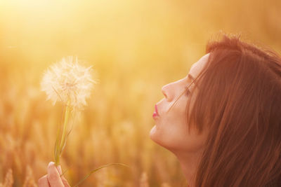 Close-up side view of woman blowing dandelion flower during sunset