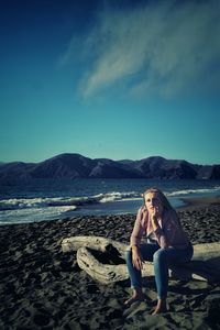 Woman sitting on shore at beach against sky