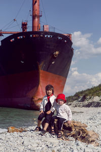 Two fashionable baby boys sit next to a large rio ship that ran aground off novorossiysk