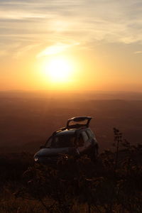 Car on landscape against sunset sky