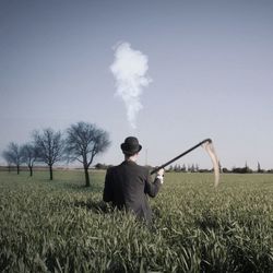 Rear view of man with scythe on field