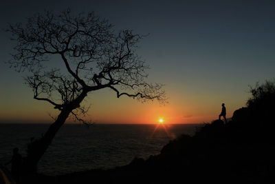 Silhouette man standing on cliff by sea against sky during sunset