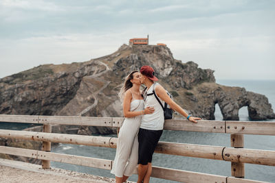 Couple embracing while standing by railing against sea