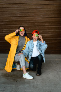 A girl in a yellow raincoat and a boy in a red cap are holding colorful ice cream in their hands