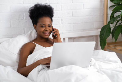 Young woman using mobile phone while sitting on bed at home