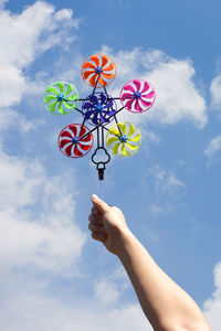 Low angle view of hand holding pinwheel toy against sky