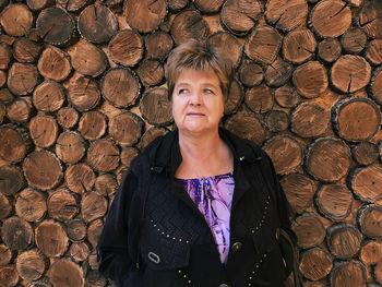 Thoughtful woman standing against stacked logs