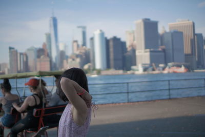 Woman standing by modern buildings in city against sky