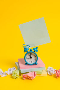 Low angle view of clock on table against yellow background