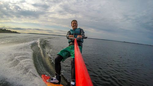 Man wakeboarding on sea against cloudy sky