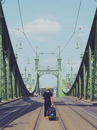 Rear view of man walking with luggage at liberty bridge