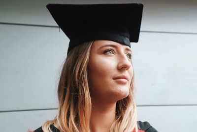 Close-up of young woman wearing mortarboard looking away while standing against wall