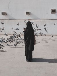 Woman standing in burka against pigeons on footpath