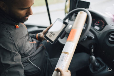 Male worker examining package while using digital tablet in delivery van