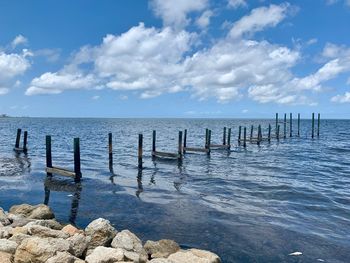 Wooden posts in sea against sky