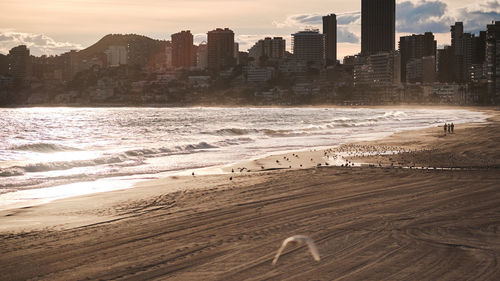 Scenic view of beach and buildings against sky during sunset