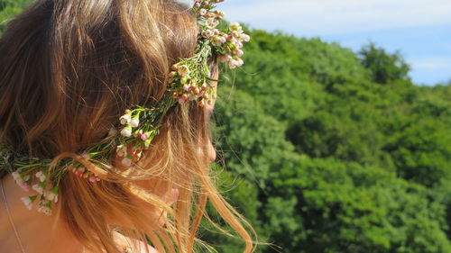 Close-up of woman wearing flowers against trees