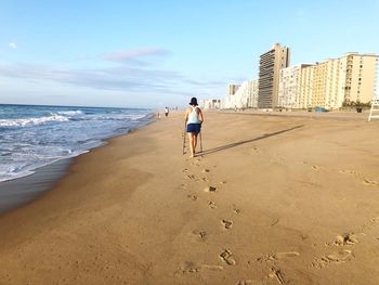 Rear view of woman with hiking pole walking on beach against sky