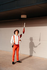 Skilled young male circus performer juggling with club on modern building