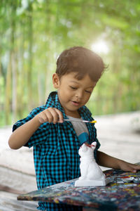 Cute boy painting figurine against trees