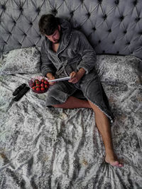 High angle view of man sitting by strawberries in bowl on bed