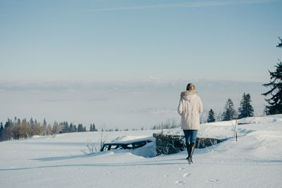 Rear view of woman walking on snow covered land against sky during winter