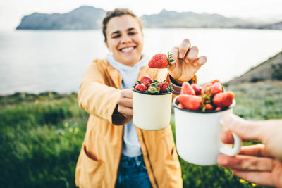 Couple smiling at camera while eating strawberries .