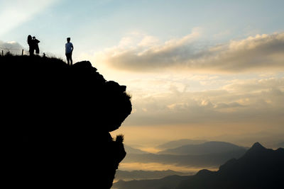 Silhouette people on rock against sky during sunset