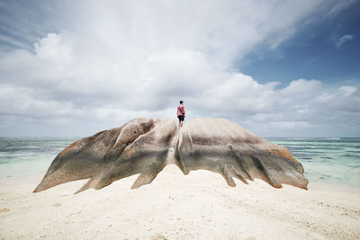 Man standing on rock and looking at view. lonely tourist enjoying calm on beach in seychelles