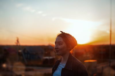 Portrait of young woman looking away against sky during sunset