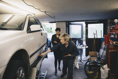 Female mechanic pointing while showing car to customer in auto repair shop