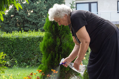 Old woman spraying garden flowers with water