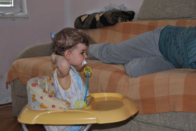 Cute baby boy sucking pacifier in walker at home