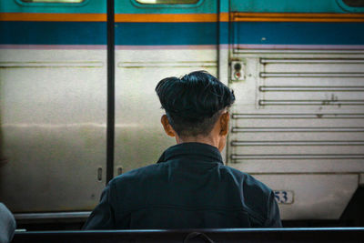 Rear view of man sitting on bench against train