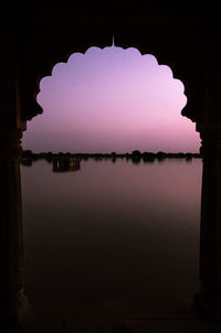 Silhouette buildings by lake against sky at night