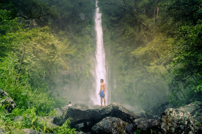 Shirtless young man standing against waterfall
