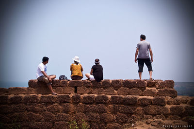 Rear view of people walking on retaining wall against clear sky