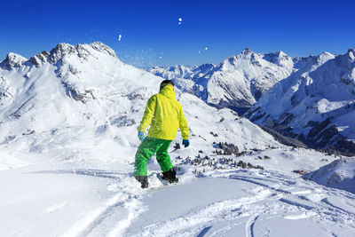 Rear view of man snowboarding on snowcapped mountain against sky
