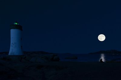 Illuminated lighthouse against blue sky at night