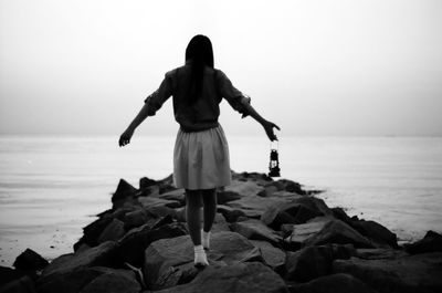 Rear view of woman on rocks by sea against sky