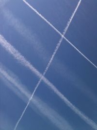 Low angle view of vapor trails in blue sky