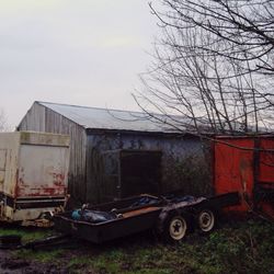 Abandoned trailer by barn on field against sky