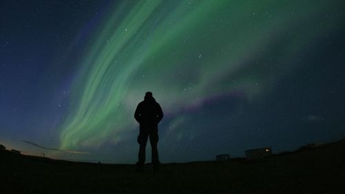 Rear view of silhouette man standing against aurora polaris