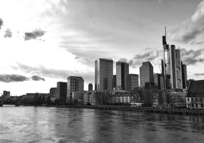 Modern buildings by river against sky in city