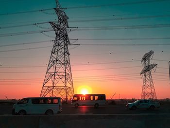 Electricity pylons against sky during sunset