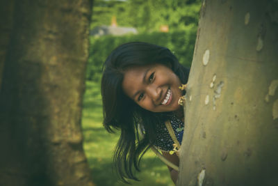 Portrait of smiling young woman standing against tree trunk