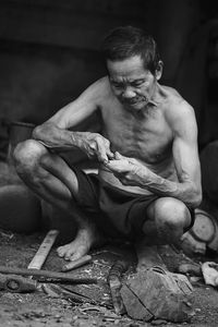 Shirtless male worker carving wood in workshop