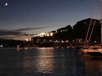 Sailboats in sea against illuminated buildings at night